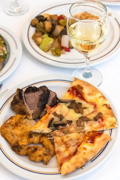 Fragment of table served with slices of pizza, meat and white wine in glass — Stock Photo, Image