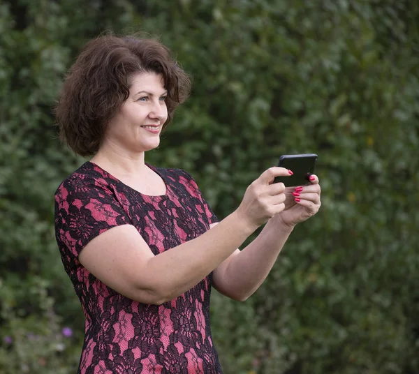 Woman looks at the phone on phone screen in nature — Stock Photo, Image