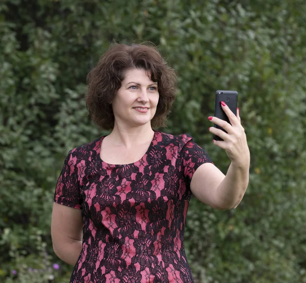 Vrouw kijkt naar de telefoon op telefoon scherm in de natuur — Stockfoto