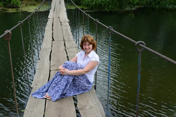 Donna seduta su un ponte di legno sul fiume — Foto Stock