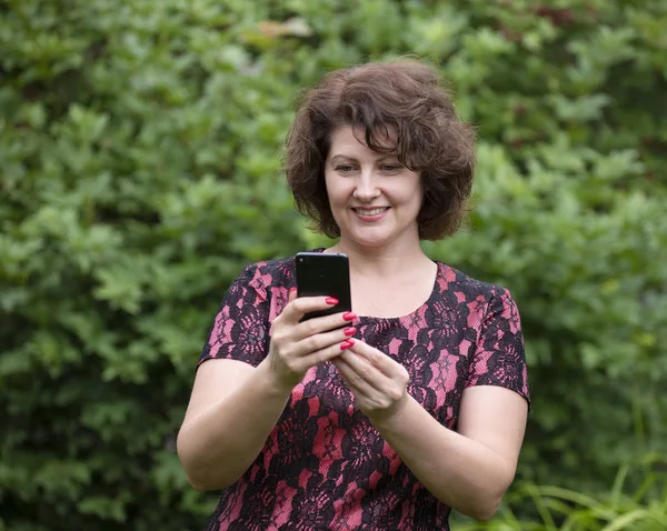 Woman looks at the phone on phone screen in nature — Stock Photo, Image