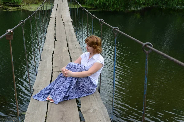 Woman sitting on a wooden bridge over the river — Stock Photo, Image