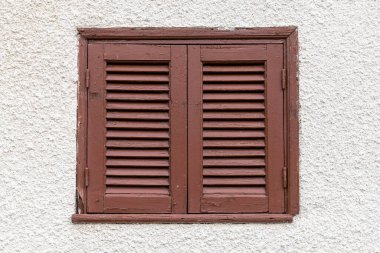 Açık bir duvarda kahverengi panjurları olan kapalı bir pencere.
