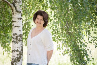 Yazın huş ağacının yanındaki Rus kadın.