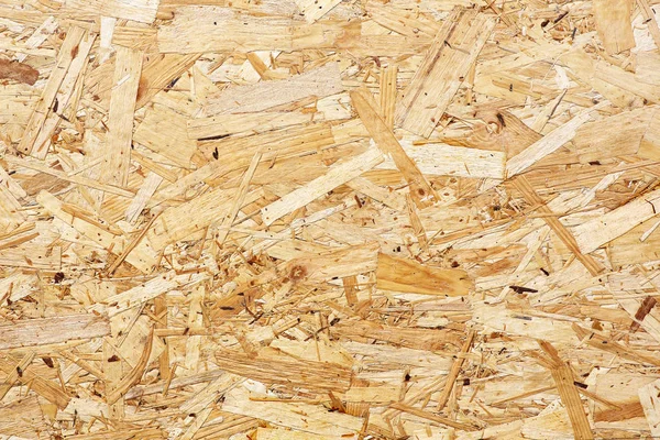 Las placas OSB están hechas de astillas de madera marrón lijadas en un fondo de madera. Vista superior del fondo de chapa de madera OSB, superficies estrechas y sin costuras . —  Fotos de Stock