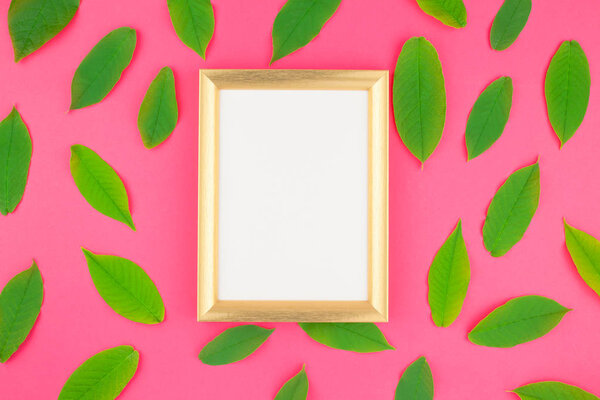 Creative flat lay top view pattern with fresh green leaves on bright pink background with golden frame mock up and copy space in minimal pop art style, template for text