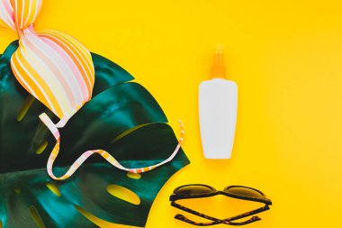 Tropikal orman palm monstera bırakır, güneş gözlüğü, güneş kremi boş şişe mockup ve kadının mayo üst parlak sarı kağıt arka plan üzerinde. Metin için yaratıcı düz yatıyordu kavramı şablon yaz tatil