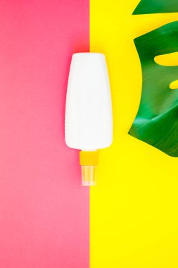 Tropikal orman palmiye monstera yaprakları ve güneş koruyucu boş şişe mockup parlak sarı ve pembe çift ton kağıt arka plan üzerinde. Metin için yaratıcı düz yatıyordu kavramı şablon yaz tatil