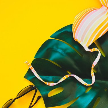 Tropikal orman palm monstera bırakır, güneş gözlüğü ve bir kadının mayo üstüne parlak kare Kağıt arka plan sarı. Metin için yaratıcı düz yatıyordu kavramı şablon yaz tatil