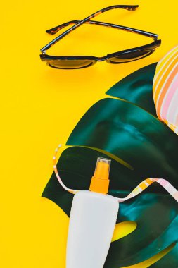 Tropikal orman palm monstera bırakır, güneş gözlüğü, güneş kremi boş şişe mockup ve kadının mayo üst parlak sarı kağıt arka plan üzerinde. Metin için yaratıcı düz yatıyordu kavramı şablon yaz tatil