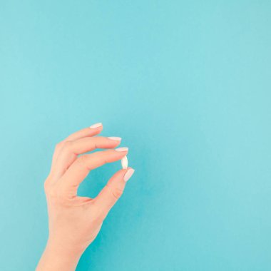 En az tarzı, kare şablon metin için kopya alanı pastel kağıt mavi zemin üzerine beyaz bir hap tutan kadın el. Tıbbi tedavi, eczane, sağlık kavramı