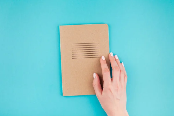 Creative flat lay of woman hands holding craft paper notebook diary with copy space on turquoise background in minimalism style. Template for feminine blog, social media