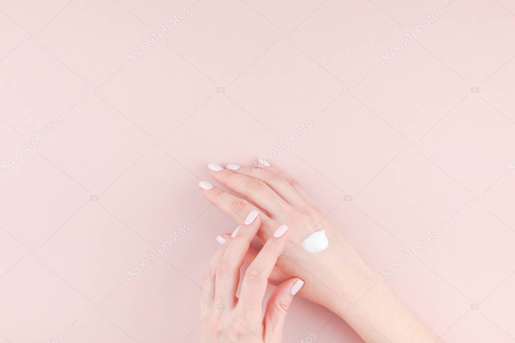 Creative image of woman moisturizing her hand with cosmetic cream lotion with copy space on millennial pink background in minimalism style. Concept template feminine blog, social media, beauty concept
