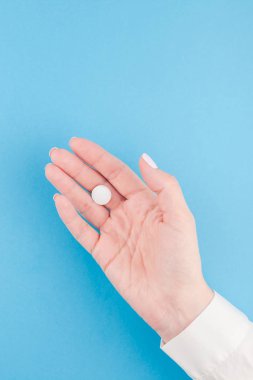 En az tarzı, şablon için metin kopya alanı pastel kağıt mavi zemin üzerine beyaz bir hap tutan kadın el. Tıbbi tedavi, eczane, sağlık kavramı.