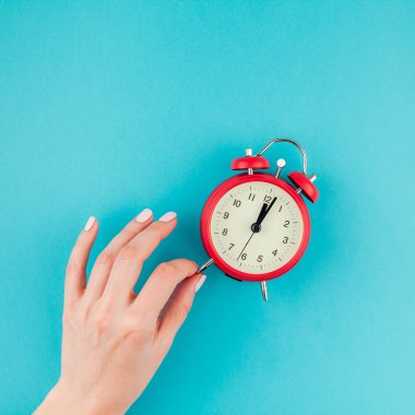 Yaratıcı düz yatıyordu kavramı kırmızı vintage çalar saat üzerinde kare parlak mavi turkuaz tutan kadın el üst görünümünü renk Kağıt arka plan kopya alanı ile en az tarzı, metin için şablon