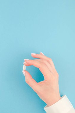 En az tarzı, şablon için metin kopya alanı pastel kağıt mavi zemin üzerine beyaz bir hap tutan kadın el. Tıbbi tedavi, eczane, sağlık kavramı.