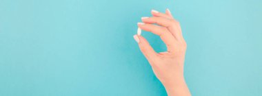 En az tarzı, şablon için metin kopya alanı pastel kağıt mavi zemin üzerine beyaz bir hap tutan kadın el. Tıbbi tedavi, eczane, sağlık kavramını. Uzun geniş afiş