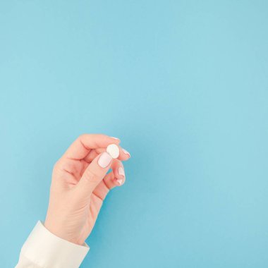 En az tarzı, kare şablon metin için kopya alanı pastel kağıt mavi zemin üzerine beyaz bir hap tutan kadın el. Tıbbi tedavi, eczane, sağlık kavramı
