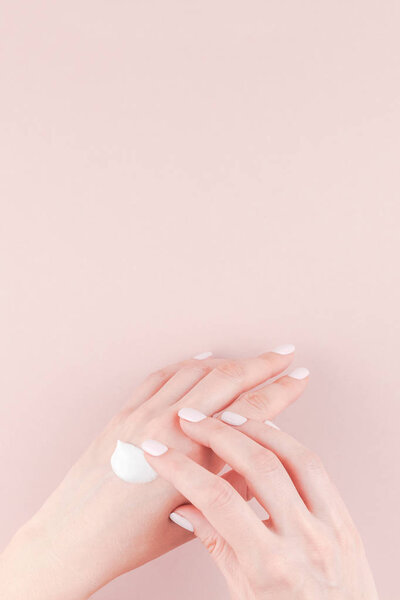 Creative image of woman moisturizing her hand with cosmetic cream lotion with copy space on millennial pink background in minimalism style. Concept template feminine blog, social media, beauty concept