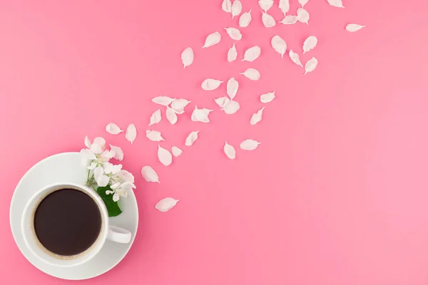 Creative flat lay concept top view of coffee cup and white apple tree flowers petals on pastel pink background with copy space in minimal style, template for text