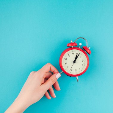 Yaratıcı düz yatıyordu kavramı kırmızı vintage çalar saat üzerinde kare parlak mavi turkuaz tutan kadın el üst görünümünü renk Kağıt arka plan kopya alanı ile en az tarzı, metin için şablon