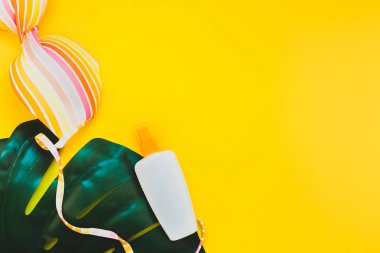 Tropikal orman palm monstera bırakır, güneş gözlüğü, güneş kremi boş şişe mockup ve kadının mayo üst parlak sarı kağıt arka plan üzerinde. Metin için yaratıcı düz yatıyordu kavramı şablon yaz tatil