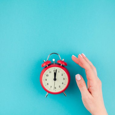 Yaratıcı düz yatıyordu kavramı kırmızı vintage çalar saat üzerinde kare parlak mavi turkuaz tutan kadın el üst görünümünü renk Kağıt arka plan kopya alanı ile en az tarzı, metin için şablon