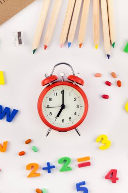 Çalar saat, renk okulu ve ofis malzemelerini kopya alanı, çerçeve, metin veya tasarım şablonu olan beyaz masa arkaplanına yerleştirerek okul kavramına yaslan