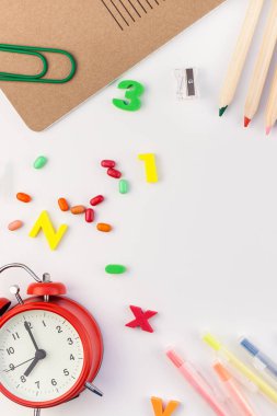 Çalar saat, renk okulu ve ofis malzemelerini kopya alanı, çerçeve, metin veya tasarım şablonu olan beyaz masa arkaplanına yerleştirerek okul kavramına yaslan