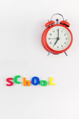 Çalar saat, renk okulu ve ofis malzemelerini kopya alanı, çerçeve, metin veya tasarım şablonu olan beyaz masa arkaplanına yerleştirerek okul kavramına yaslan