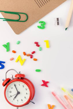 Çalar saat, renk okulu ve ofis malzemelerini kopya alanı, çerçeve, metin veya tasarım şablonu olan beyaz masa arkaplanına yerleştirerek okul kavramına yaslan