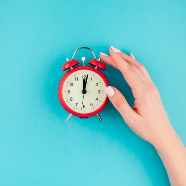 Yaratıcı düz yatıyordu kavramı kırmızı vintage çalar saat üzerinde kare parlak mavi turkuaz tutan kadın el üst görünümünü renk Kağıt arka plan kopya alanı ile en az tarzı, metin için şablon