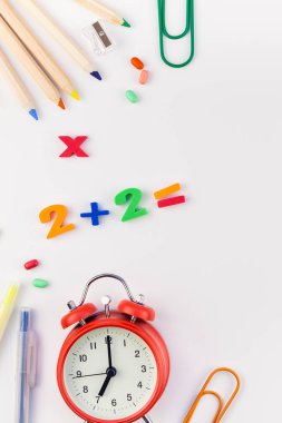 Çalar saat, renk okulu ve ofis malzemelerini kopya alanı, çerçeve, metin veya tasarım şablonu olan beyaz masa arkaplanına yerleştirerek okul kavramına yaslan