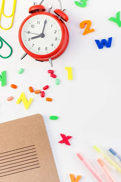 Çalar saat, renk okulu ve ofis malzemelerini kopya alanı, çerçeve, metin veya tasarım şablonu olan beyaz masa arkaplanına yerleştirerek okul kavramına yaslan