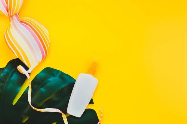 Tropikal orman palm monstera bırakır, güneş gözlüğü, güneş kremi boş şişe mockup ve kadının mayo üst parlak sarı kağıt arka plan üzerinde. Metin için yaratıcı düz yatıyordu kavramı şablon yaz tatil