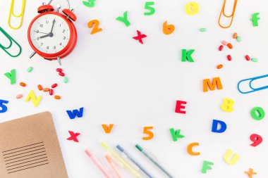 Çalar saat, renk okulu ve ofis malzemelerini kopya alanı, çerçeve, metin veya tasarım şablonu olan beyaz masa arkaplanına yerleştirerek okul kavramına yaslan