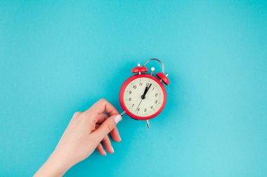 Yaratıcı düz yatıyordu kavramı kırmızı vintage çalar saat parlak mavi turkuaz üzerinde tutan kadın el üst görünümünü renk Kağıt arka plan kopya alanı ile en az tarzı, metin için şablon