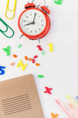 Çalar saat, renk okulu ve ofis malzemelerini kopya alanı, çerçeve, metin veya tasarım şablonu olan beyaz masa arkaplanına yerleştirerek okul kavramına yaslan
