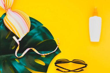 Tropikal orman palm monstera bırakır, güneş gözlüğü, güneş kremi boş şişe mockup ve kadının mayo üst parlak sarı kağıt arka plan üzerinde. Metin için yaratıcı düz yatıyordu kavramı şablon yaz tatil