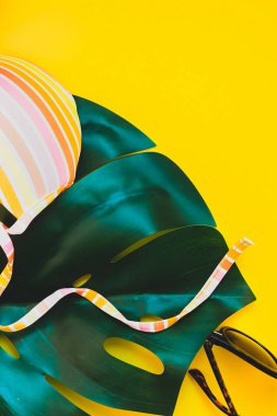 Tropikal orman palm monstera, güneş gözlüğü ve parlak sarı kağıt arka plan bir kadının mayo üstüne bırakır. Metin için yaratıcı düz yatıyordu kavramı şablon yaz tatil