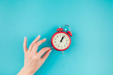 Yaratıcı düz yatıyordu kavramı kırmızı vintage çalar saat parlak mavi turkuaz üzerinde tutan kadın el üst görünümünü renk Kağıt arka plan kopya alanı ile en az tarzı, metin için şablon