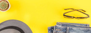 Düz mavi jeans, gri şapka, kaktüs ve akıllı telefon kulaklık kalın sarı Kağıt arka plan üzerinde kopya alanı ile yatıyordu. Kadın rahat kıyafet havai görünümü. Uzun geniş afiş