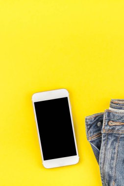 Düz mavi kot pantolon ve smartphone kalın sarı Kağıt arka plan kopya alanı ile kulaklıktan yatırın. Kadın rahat kıyafet havai görünümü. Trendy hipster bak üstten görünüm