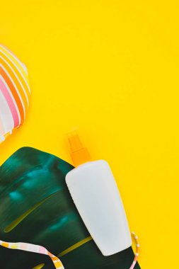 Tropikal orman palm monstera bırakır, güneş gözlüğü, güneş kremi boş şişe mockup ve kadının mayo üst parlak sarı kağıt arka plan üzerinde. Metin için yaratıcı düz yatıyordu kavramı şablon yaz tatil