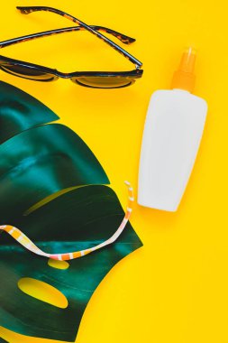 Tropikal orman palm monstera bırakır, güneş gözlüğü, güneş kremi boş şişe mockup ve kadının mayo üst parlak sarı kağıt arka plan üzerinde. Metin için yaratıcı düz yatıyordu kavramı şablon yaz tatil