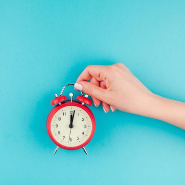 Yaratıcı düz yatıyordu kavramı kırmızı vintage çalar saat üzerinde kare parlak mavi turkuaz tutan kadın el üst görünümünü renk Kağıt arka plan kopya alanı ile en az tarzı, metin için şablon