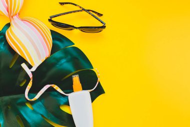 Tropikal orman palm monstera bırakır, güneş gözlüğü, güneş kremi boş şişe mockup ve kadının mayo üst parlak sarı kağıt arka plan üzerinde. Metin için yaratıcı düz yatıyordu kavramı şablon yaz tatil