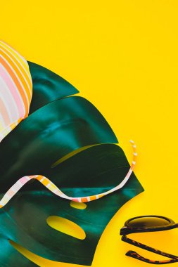 Tropikal orman palm monstera bırakır, güneş gözlüğü, güneş kremi boş şişe mockup ve kadının mayo üst parlak sarı kağıt arka plan üzerinde. Metin için yaratıcı düz yatıyordu kavramı şablon yaz tatil