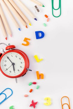 Çalar saat, renk okulu ve ofis malzemelerini kopya alanı, çerçeve, metin veya tasarım şablonu olan beyaz masa arkaplanına yerleştirerek okul kavramına yaslan