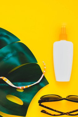 Tropikal orman palm monstera bırakır, güneş gözlüğü, güneş kremi boş şişe mockup ve kadının mayo üst parlak sarı kağıt arka plan üzerinde. Metin için yaratıcı düz yatıyordu kavramı şablon yaz tatil